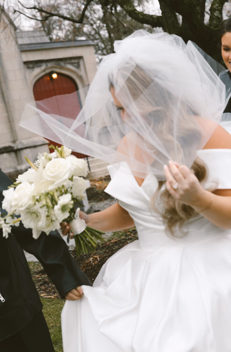 A bride having her long veil adjusted outdoors