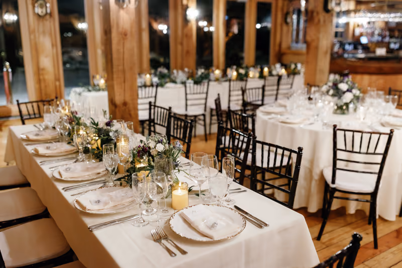 A close-up of a set reception table in a wooden room, decorated with white floral centerpieces and candles