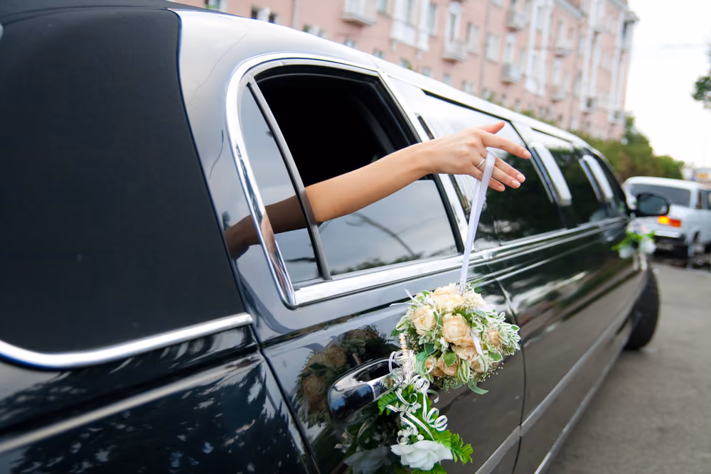 A hand holding a white ribbon out the window of a black wedding limousine